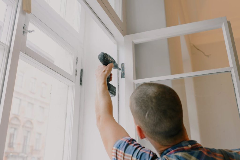 anonymous-man-installing-window-in-room-5691503 A handyman works with a drill installing window hinges indoors.