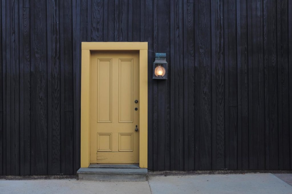 closed-door-and-lighted-light-sconce-277559 A modern yellow door on a dark wooden facade creates a striking contrast. Architectural detail.